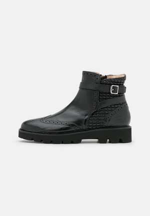 Sort læderankelstøvle med brogue-detaljer, tekstureret hæl, rem med metalspænde og tyk sål med kraftigt mønster.