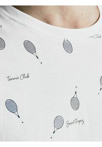 Bílé bavlněné tričko s opakujícím se vzorem černých tenisových raket a texty "Tennis Club" a "Saint-Tropez" v kurzívě.