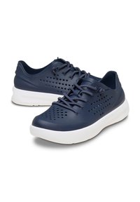 Zapatillas de deporte azul marino con parte superior perforada, suela blanca y cordones a juego; diseñadas para la transpirabilidad y la comodidad. Forma redondeada y acentos texturizados.