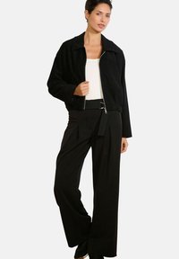 Čierna krátka bunda so širokým golierom, zapínaním na zips a čierne plisované nohavice. Oblečenie obsahuje biely top a voľný strih.