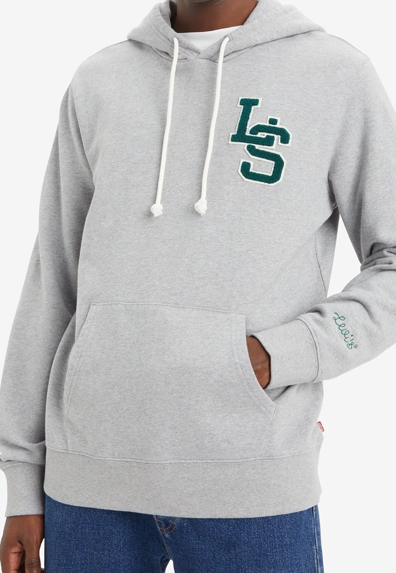 Sudadera gris con capucha, que presenta un logo verde bordado en el pecho, detalles con cordón y un bolsillo canguro en la parte delantera.