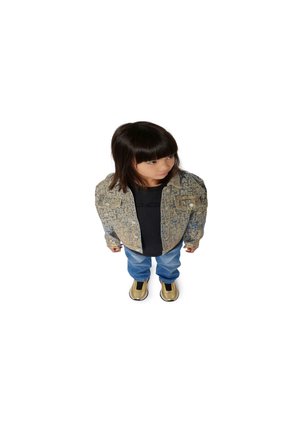 Veste en denim avec impression de texte, T-shirt noir, jeans bleus et chaussures gold à enfiler. Posture debout, regardant légèrement sur le côté.