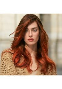 Lang, golvend haar in een levendige rode kleur met donkere wortels. Gedragen met een beige, gebreide trui met een ingewikkeld open geweven patroon.
