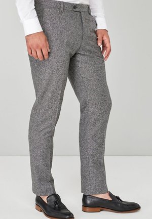 Pantalon en tweed gris avec une coupe slim, devant plat et poches, associé à des chaussures en cuir noires. Le tissu a une finition texturée.