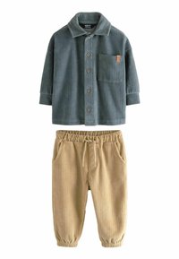 Tummanvihreä corduroy-paita, jossa on napit ja tasku; yhdistetty vaaleanbeigeihin corduroy-housuihin, joissa on elastinen vyötärö ja hihnat.