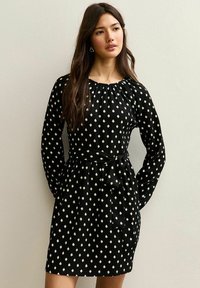 Vestido negro de manga larga, con acentos de patrón de diamantes blancos, escote fruncido y un cinturón atado a la cintura. Tela texturizada.