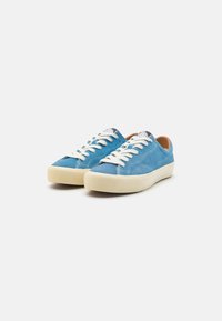 Sneakers azul de camurça com atacadores brancos, solas de borracha creme e detalhes de costura sutis. Bico redondo e etiqueta de calcanhar com marca.