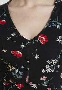 Černé květinové šaty s červenými a bílými květinovými vzory, s výstřihem do V, malými knoflíčky podél těla a hladkým textilním povrchem.