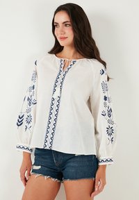Valge linane pluus, millel on tumesinised lillemustrid varrukatel ja keskpaneelil on nööpaukudega kaelus. Kombineeritud denim-lühikesed püksid.