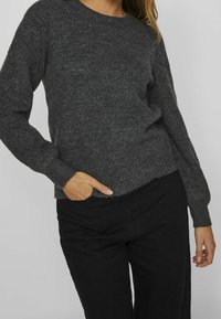 Pull gris foncé en maille avec manches longues et encolure ronde. Présente une texture côtelée et une coupe légèrement courte. Design décontracté.