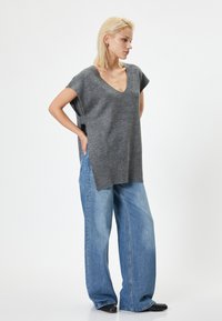 Top grigio lavorato a maglia con scollo a V e maniche corte, abbinato a jeans in denim azzurri larghi. Le fessure laterali aggiungono dettaglio al design.