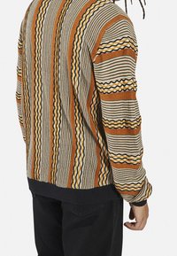 Knit sweater with multi-colored striped pattern in brown, beige, and blue. Ribbed cuffs and hem complete the relaxed fit design.