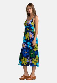 Blumenkleid mit dunklem blauen Hintergrund, das große grüne, blaue und lila Blumen zeigt. Spaghettiträger und mittellanges Design.