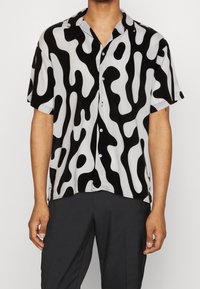 Camicia a maniche corte in bianco e nero con motivo astratto a onde; il tessuto è liscio; presenta una chiusura con bottoni e un colletto classico.