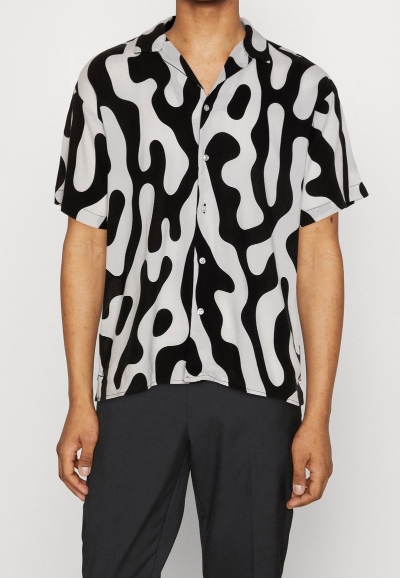 Camicia a maniche corte in bianco e nero con motivo astratto a onde; il tessuto è liscio; presenta una chiusura con bottoni e un colletto classico.