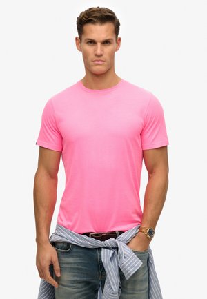 Bright pink short-sleeve t-shirt made of a soft material, featuring a round neckline. Paired with blue jeans and a light blue striped shirt tied at the waist.