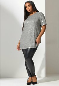 Top de lentejuelas plateadas con mangas cortas, de corte relajado. Combinado con leggings de cuero sintético negros y tacones negros. Textura suave, superficie brillante.