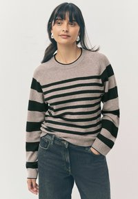 Un pull gris clair avec des rayures horizontales noires, un col rond et des poignets côtelés. Porté avec un jean en denim foncé. Texture douce.