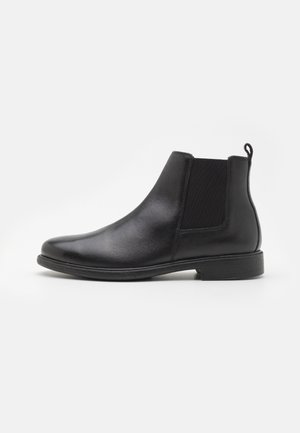 Botte Chelsea en cuir noir avec panneau latéral élastique et languette, talon bas et bout arrondi sur fond blanc.