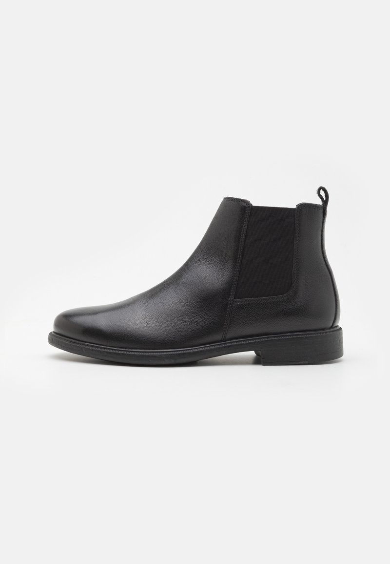 Botte Chelsea en cuir noir avec panneau latéral élastique et languette, talon bas et bout arrondi sur fond blanc.