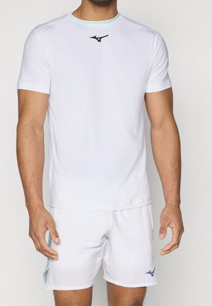 Mężczyzna noszący biały sportowy t-shirt z krótkim rękawem i pasujące szorty z czarnymi logo marki sportowej na piersi i lewej nodze.