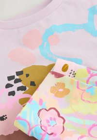 Īss piedurkņu lavandas krāsas T-krekls ar daudzkrāsainiem ziedu rakstiem, kopā ar rakstainu audumu, kam ir pasteļtoņi un dažādas formas.