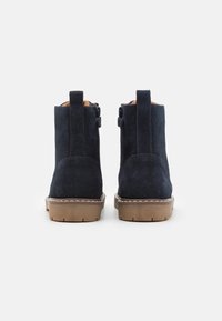 Námořnické semišové kotníkové boty s hnědou gumovou podrážkou, vertikálními bočními zipy a smyčkovými poutky na zadní straně. Hladký povrch s jemným leskem.