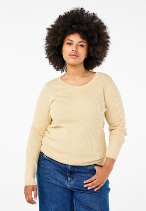 Pull long à manches longues beige côtelé avec un col scallopé et une silhouette ajustée. Porté avec un jean bleu taille haute, mettant en avant un matériau texturé.