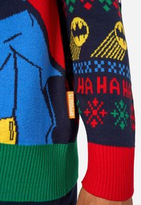 Tumesinine kampsun, millel on sinine koomiksikujuline figuur kollase vöökohaga, punased ja rohelised soonikkoes varrukasäärised ning pidulikud mustrid kollases, punases ja rohelises.