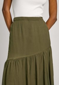 Jupe fluide vert olive en tissu texturé. Caractéristiques : volants froncés au bas et ceinture élastique. Pas de motif visible.