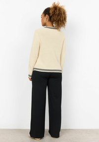 Maglione a maglia beige con colletto a righe bianche e nere, abbinato a pantaloni neri a gamba larga. La texture è a costine, per un look informale.