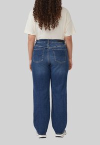 Blaue Jeans aus Denim mit hoher Taille und weitem Bein, ausgestattet mit zwei Gesäßtaschen und einer genähten Nahtdetails. Kombiniert mit einem hellen Oberteil.