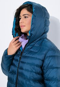 Chaqueta acolchada de color marino con acabado brillante, que cuenta con una capucha forrada en teal. Parte delantera con cremallera y costuras acolchadas horizontales para mayor aislamiento.