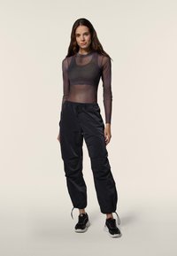 Schwarze, leichte Cargohosen mit verstellbaren Bündchen, kombiniert mit einem schwarzen transparenten Langarmshirt mit Rundhalsausschnitt.