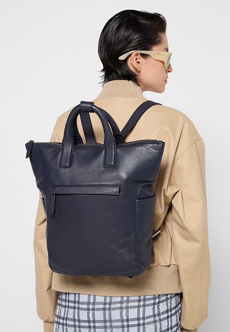 Granatowy skórzany plecak z podwójnymi górnymi uchwytami i regulowanymi paskami na ramiona. Posiada przednią kieszeń na zamek i elegancki, minimalistyczny design.