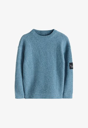 Blauer strukturierter Strickpullover mit Rundhalsausschnitt, kombiniert mit locker sitzenden dunkelgrauen Jeans und weißen Turnschuhen.