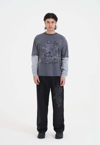 Grijs langarm shirt met grafische print, gecombineerd met zwarte brede broek met een drakendesign. Schoenen zijn zwart en gestructureerd.