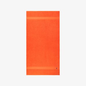 Φωτεινή πορτοκαλί πετσέτα από πετσέτα terry, με απαλό υφή και οριζόντια ταινία στο πάνω μέρος. Μικρό μπλε λογότυπο στο κάτω μέρος.