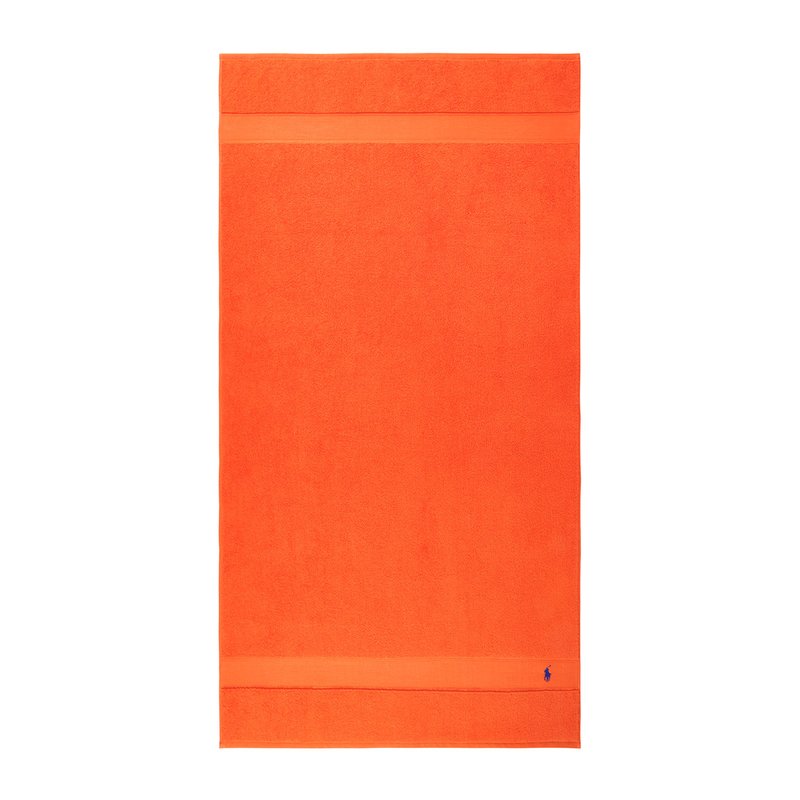 Φωτεινή πορτοκαλί πετσέτα από πετσέτα terry, με απαλό υφή και οριζόντια ταινία στο πάνω μέρος. Μικρό μπλε λογότυπο στο κάτω μέρος.