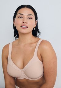 Light beige smooth fabric bra with wide straps, underwire support, and textured panels. Simple design with no visible hardware or embellishments.