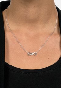 Silver infinity necklace featuring a twisted design with embedded clear crystals. Chain is thin and delicate, complementing the pendant.