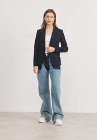 Námořnický blazer s přizpůsobeným střihem, zapínání na jeden knoflík, kombinovaný se světle modrými širokými džíny a bílými teniskami. Hladká tkanina, strukturovaný střih.