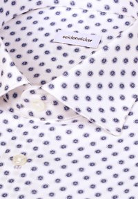 Camicia bianca da uomo con un piccolo motivo a pois blu navy, dotata di colletto classico, chiusure con bottoni e etichetta seidensticker vicino al colletto.