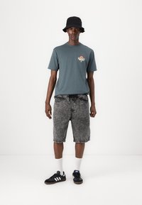 Gray t-shirt with a small graphic on the chest, black denim shorts, white crew socks, and black sneakers with three white stripes. Black bucket hat.