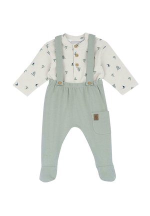 Salopette di cotone verde chiaro con bretelle, accompagnata da una camicia a maniche lunghe a fantasia con piccoli motivi di veliero e foglie. Chiusura a bottone e tasca laterale.