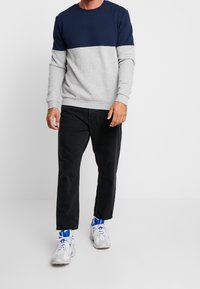 Sudadera bloqueada en colores navy y gris claro con mangas largas, cuello redondo y puños acanalados, combinada con pantalones negros y zapatillas blancas.