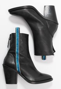 Bottes chevilles en cuir noir avec un bout effilé et un talon épais. Présentent une bande bleue et argentée le long de la fermeture éclair et des accents texturés.