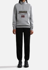 Felpa grigia con zip e colletto alto, caratterizzata da una grande toppa nera e una bandiera della Norvegia. Abbinata a pantaloni jogger neri e sneakers nere.