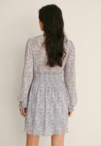 Světlomodré květinové šaty s dlouhými rukávy a nařaseným pasem. Vyrobené z texturované látky s volánkovým zakončením. Detaily s vlnkovanými manžetami.