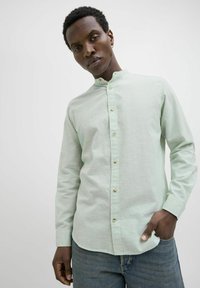 Cămașă verde mentă, cu mânecă lungă, guler mandarin, față cu butoane și țesătură texturată. Asortată cu blugi pentru un look casual.
